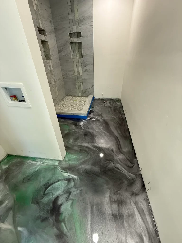 Gray and green metallic epoxy bathroom floor beside a tiled shower